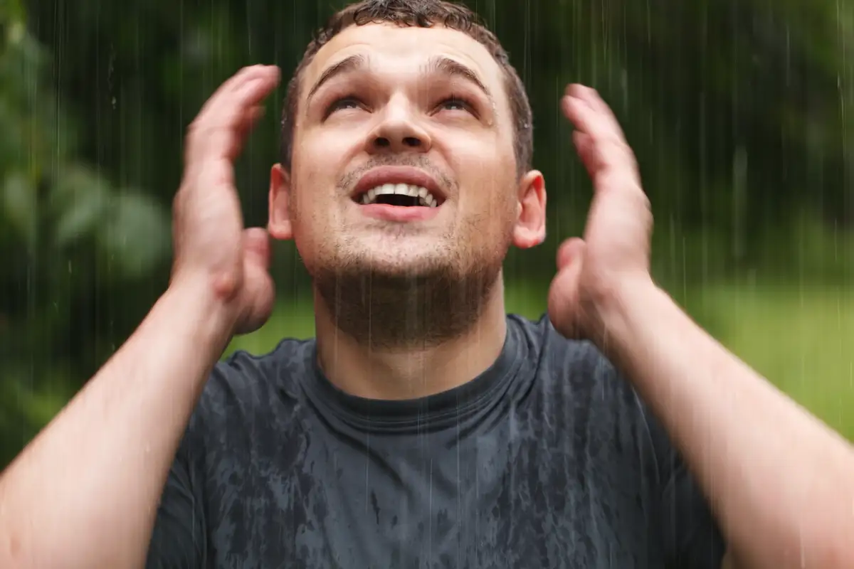 A man standing in the rain with a smile, looking upward, representing faith, endurance, and spiritual growth through trials